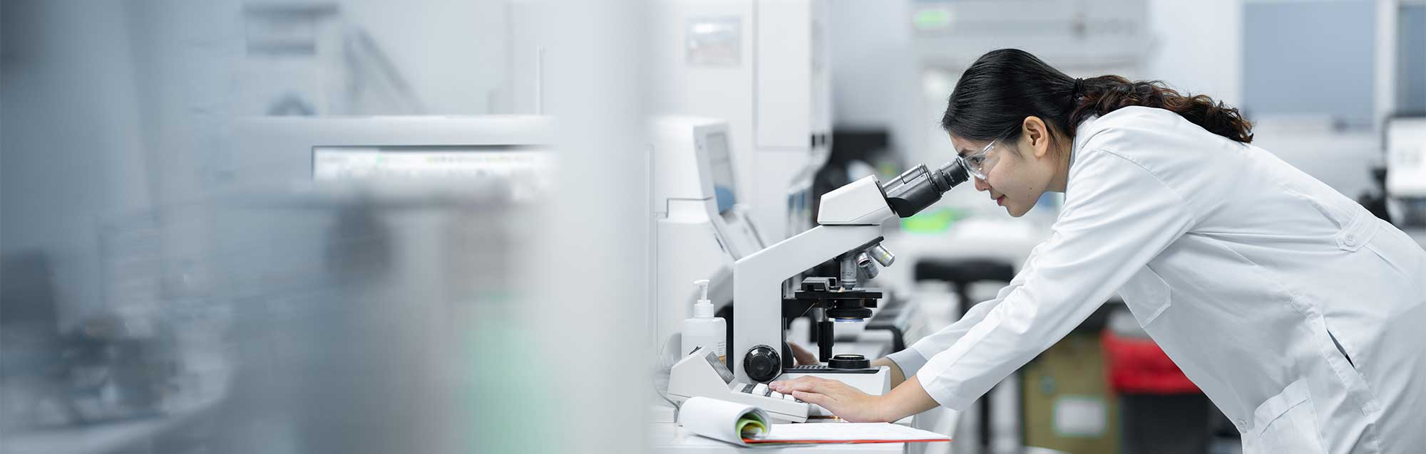Lady in lab coat looking through microscope and using lab equipment